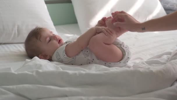 Un bambino con un pannolino giace su un letto bianco, con un letto color menta sullo sfondo. - Filmati, video