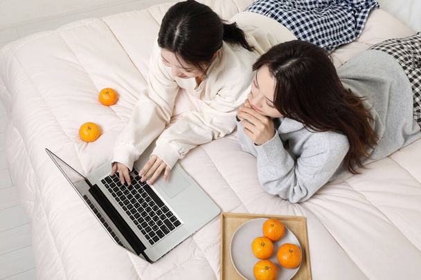 winter season concept, two beautiful Asian Korean women watching laptop videos while eating tea and fruits on bed - Foto, immagini