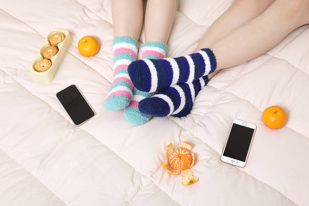 winter season concept, two beautiful Asian Korean women wearing fruit snacks, smartphones, and sleeping socks - Фото, изображение