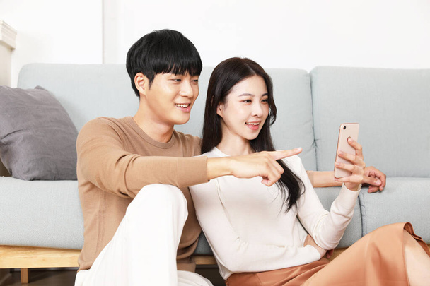 Asian Korean couple having cozy time with smart phone, winter home date concept - Foto, immagini