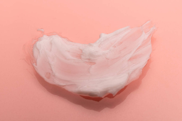 Frottis blanc de crème cosmétique isolé sur fond rose. Texture de fond de teint crémeuse. Frottis de crème pour le visage. Texture de fond crème - Photo, image