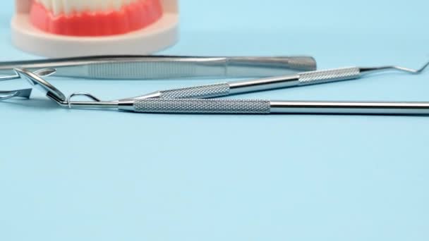 modelo plástico de la mandíbula con dientes blancos y diversos instrumentos dentales para el trabajo del médico en la cavidad oral, fondo azul, movimiento de la cámara de derecha a izquierda - Metraje, vídeo