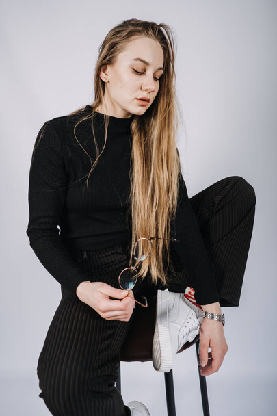 Studio candid unaltered portrait of young blonde woman with long hair sitting on chair. Portrait of Fashionable stylish blonde long hair girl in casual style cloth. - Фото, зображення