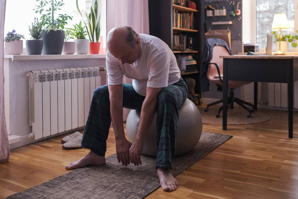 Hombre mayor haciendo ejercicios con pelota de fitness en casa estirando los músculos. - Foto, Imagen