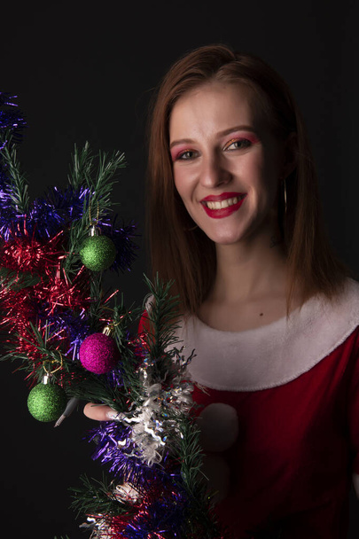 Cheerful girl in red Christmas Santa costume posing with decorated Christmas tree in studio - Фото, зображення