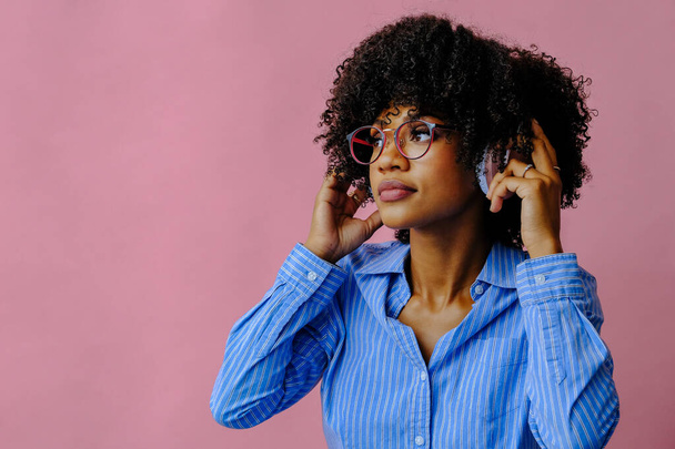 όμορφη νεαρή Αφροαμερικανή γυναίκα ακούγοντας μουσική σε ακουστικά που απομονώνονται σε ροζ φόντο - Φωτογραφία, εικόνα