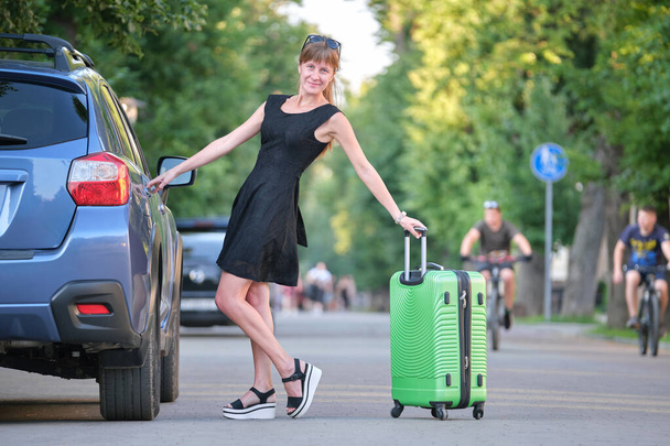 Mujer joven y feliz con la maleta de pie cerca de su coche durante el viaje por carretera. Concepto de viajes y vacaciones - Foto, Imagen