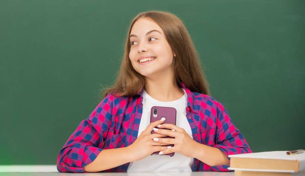niño feliz en la escuela charlando por teléfono en el fondo de pizarra, mensaje - Foto, imagen