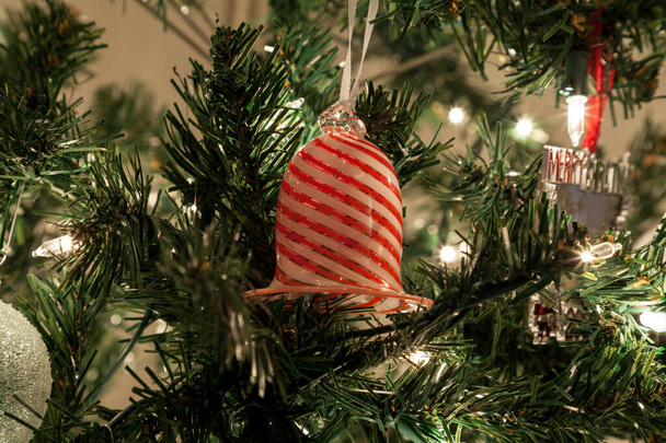 Ornement de cloche de Noël en verre blanc et rouge accroché sur un arbre avec des lumières blanches autour de la saison des fêtes. - Photo, image