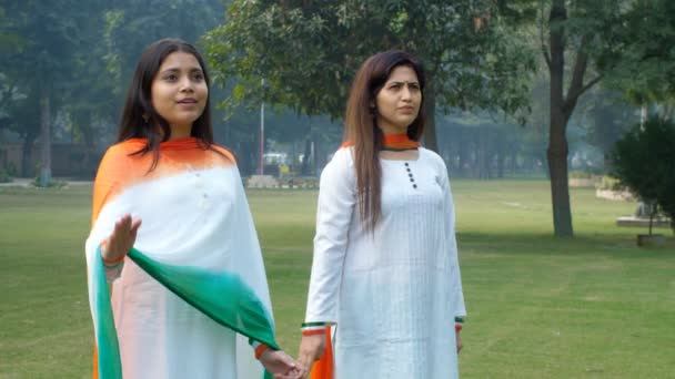 Duas jovens mulheres saudam alegremente a Bandeira Nacional Indiana enquanto estão juntas. Mulheres patrióticas vestindo Kurtis branco tradicional com Dupattas Tricolored em celebrações República / Dia da Independência orgulho, herança cultural, patriotismo - Filmagem, Vídeo