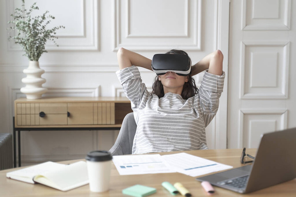 Jong blij vrouw kantoormedewerker in virtual reality bril op de werkplek, ontspannen in VR helm op het werk - Foto, afbeelding