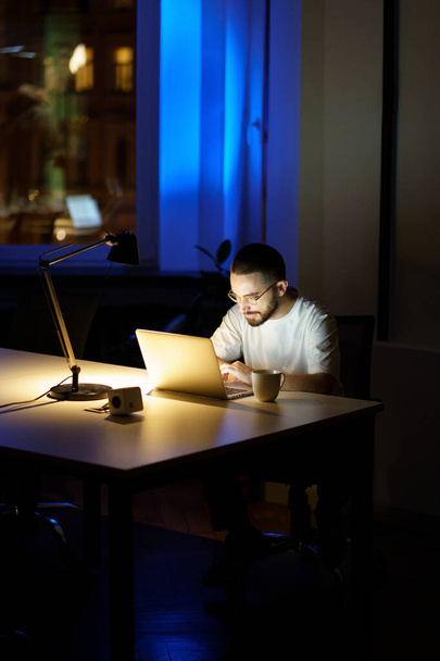 Bedachtzame jonge zakenman in bril werken op laptop 's nachts voor te bereiden voor het opstarten presentatie - Foto, afbeelding