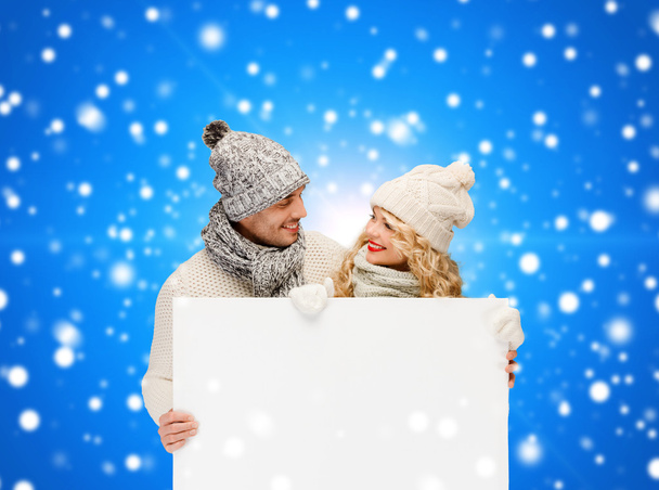 smiling couple in winter clothes with white board - Фото, изображение