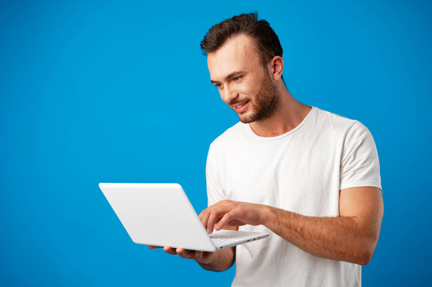 Handsome young man using his laptop against blue background - Photo, Image
