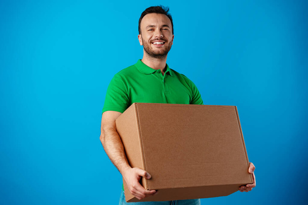 Delivery man with box in studio against blue background - Fotografie, Obrázek