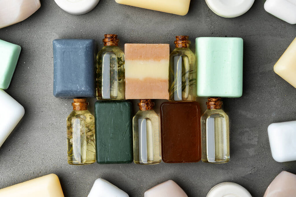 Bottles of essential oil and soap bars on gray background - Фото, изображение