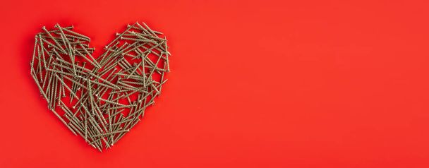 Metal nails laid out randomly in shape of heart on red background. Broken heart relation concept. Copy space. Banner - Фото, изображение