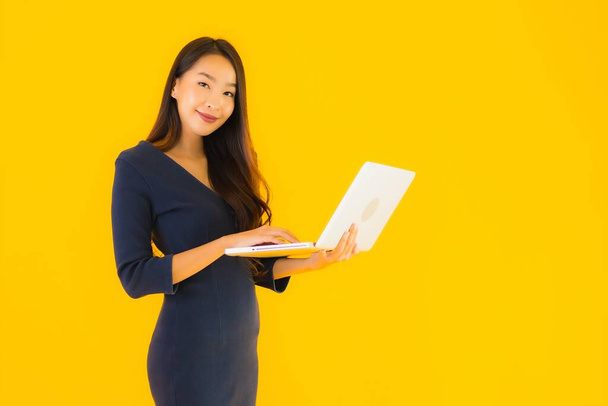 Portrait beautiful young asian woman with laptop or computer on yellow isolated background - Foto, afbeelding