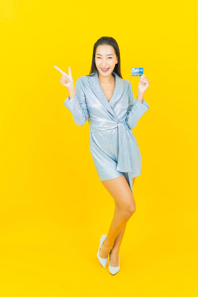 Retrato hermosa joven mujer asiática sonrisa con tarjeta de crédito sobre fondo de color amarillo - Foto, imagen