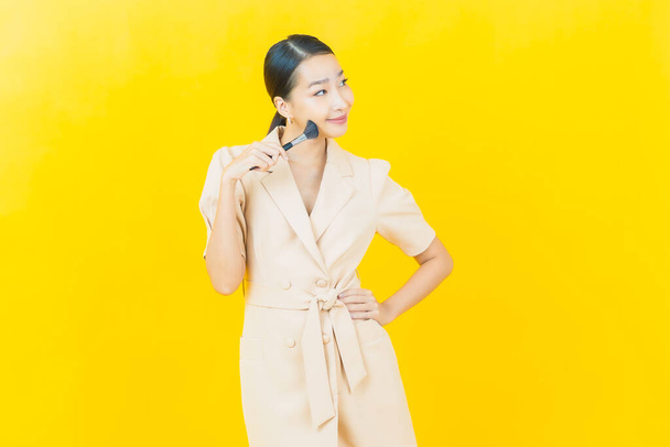 Portret mooie jonge aziatische vrouw met make-up borstel cosmetische op kleur achtergrond - Foto, afbeelding