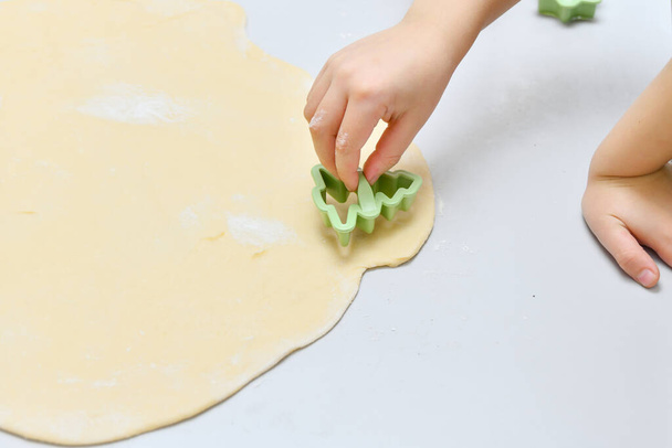 Ein Kind mit kleinen Händen fertigt aus ausgerolltem Teig verschiedene Figuren für das Backen im Ofen. - Foto, Bild