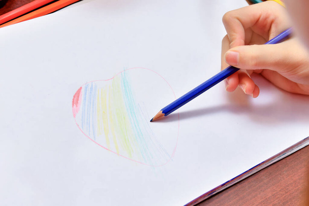 Девушка рисует сердце цветными карандашами на белом листе бумаги. - Фото, изображение