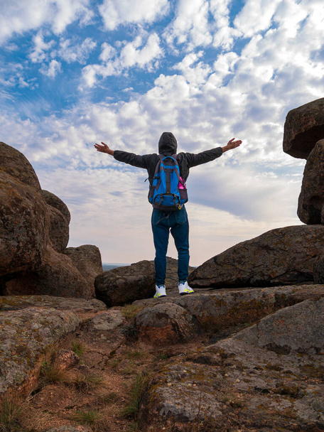 Traveler πεζοπόρος άνθρωπος με σακίδιο σήκωσε τα χέρια στην κορυφή του βουνού απολαμβάνοντας εναέρια θέα μπλε συννεφιασμένο ουρανό πίσω άποψη. Ενεργός τουρισμός Lifestyle Solo Travel Γραφικό τοπίο πεζοπορική διαδρομή Backpacking ακραία - Φωτογραφία, εικόνα