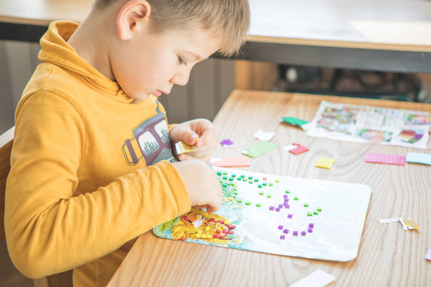 A kisfiú kreatív, hogy házi készítésű csináld magad dinoszaurusz mozaik. A kreativitás támogatása, cselekvéssel történő tanulás, tapasztalatokon keresztüli tanulás. A gyermekek kreatív látásmódhoz való hozzáférésének elősegítése. - Fotó, kép