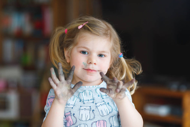 Söpö suloinen vauva tyttö oppimisen maalaus vesiväreillä. Pieni lapsi piirustus kotona, käyttäen värikkäitä harjat. Terve onnellinen lapsi, jolla on likaiset kasvot ja kädet kotona tai lastentarhassa - Valokuva, kuva