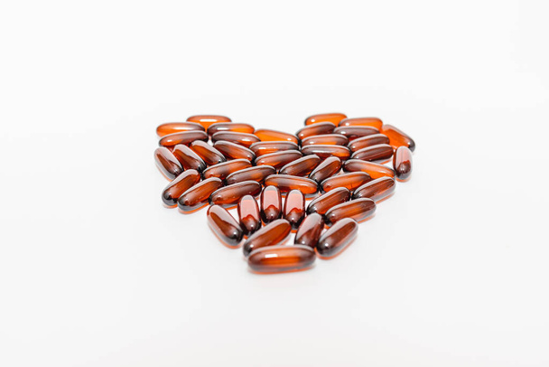 Olie bruine hartvorm pillen D3 op de witte achtergrond. Flat lay capsules vitamine D close-up, selectieve focus.. - Foto, afbeelding