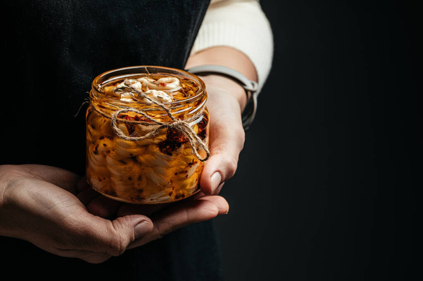 Woman hands holds glass jar with cheese in olive oil and aromatic herbs on a dark background. banner, menu, recipe place for text. - Фото, зображення
