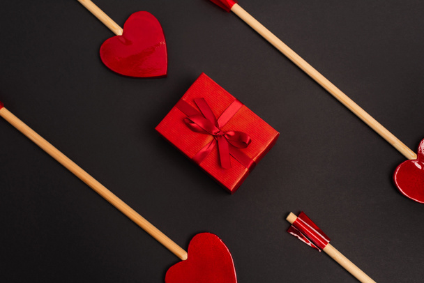 top view of heart-shaped arrows near wrapped present on black  - Φωτογραφία, εικόνα