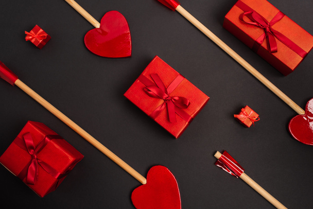 top view of heart-shaped arrows near wrapped presents on black  - Foto, Bild