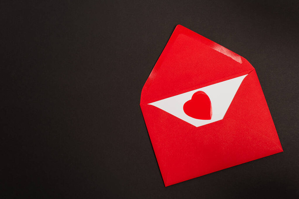 vue du dessus de l'enveloppe rouge avec lettre d'amour et coeur coupé en papier isolé sur noir  - Photo, image