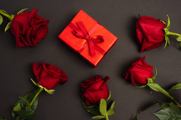 flat lay of red roses near wrapped gift box on black  - Photo, Image