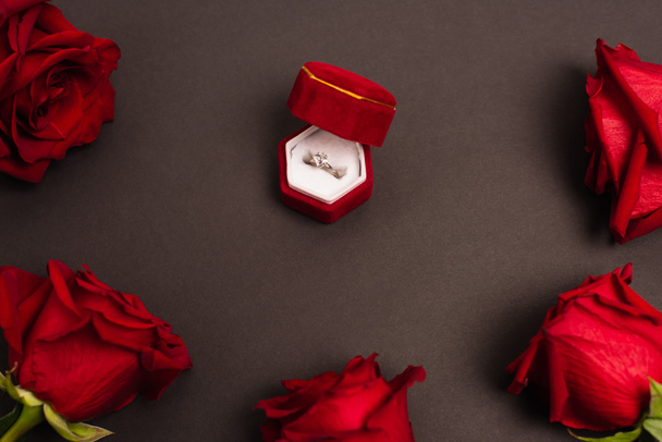 top view of jewelry box with diamond ring near red roses on black - Фото, зображення
