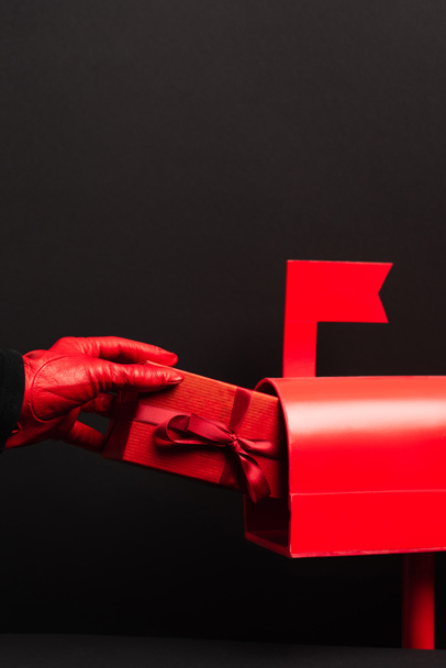 Kırmızılı kişinin kırpılmış görüntüsü siyah üzerine izole edilmiş posta kutusuna sarılı hediyeyi koyuyor  - Fotoğraf, Görsel