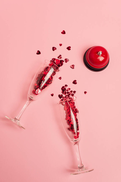 top view of champagne glasses with confetti hearts near metallic bell on pink - 写真・画像