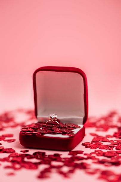 close up of jewelry box with diamond ring near shiny confetti hearts on pink - Fotografie, Obrázek