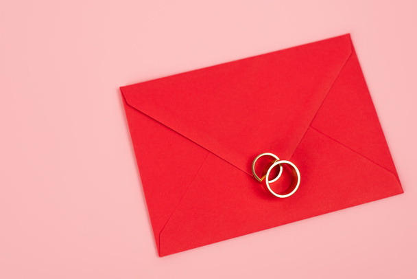 bovenaanzicht van ringen op rode envelop geïsoleerd op roze  - Foto, afbeelding