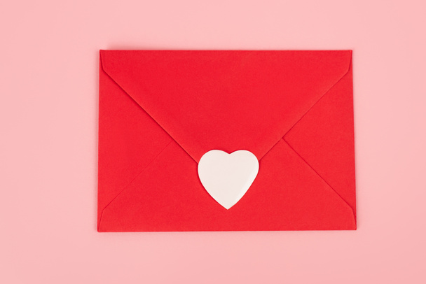 vista superior de la etiqueta engomada corazón de papel en sobre rojo aislado en rosa  - Foto, Imagen