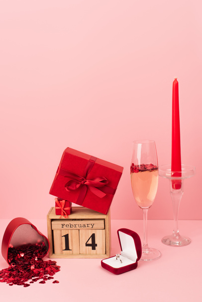 cajas de regalo rojas en el calendario con 14 febrero cerca de champán en vidrio, anillo de compromiso, vela y confeti en rosa - Foto, Imagen