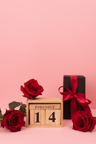 present and red roses near wooden cubes with 14 february lettering on pink  - Foto, Imagen
