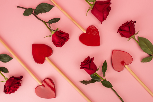 flat lay of heart-shaped lollipops near red roses on pink - Fotoğraf, Görsel