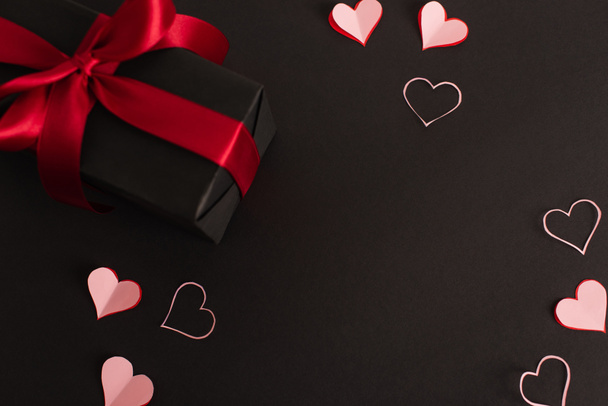 top view of pink paper cut hearts near wrapped present on black - Valokuva, kuva