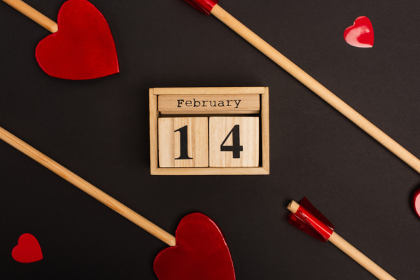 top view of wooden calendar with 14 february near heart-shaped lollipops on black - Fotografie, Obrázek