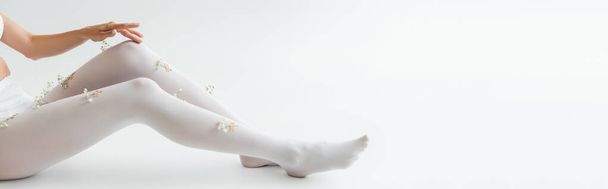 cropped view of woman with tiny flowers on tights sitting on light grey background, banner - Foto, afbeelding