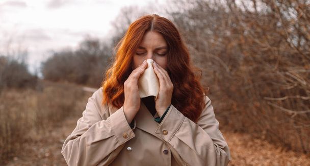 Sonbahar parkında mendili akan hasta bir genç kadın soğuk burun enfeksiyonu. Sağlık, soğuk, alerji konsepti - Fotoğraf, Görsel