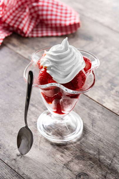 Strawberries and whipped cream in ice cream glass on wooden table - Photo, Image