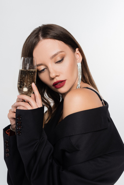 seductive brunette woman in black blazer holding glass of champagne isolated on grey - Fotoğraf, Görsel